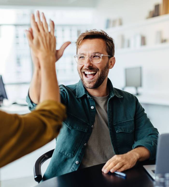 Symbolbild: Frau und Mann klatschen sich im Büro ab und lachen.