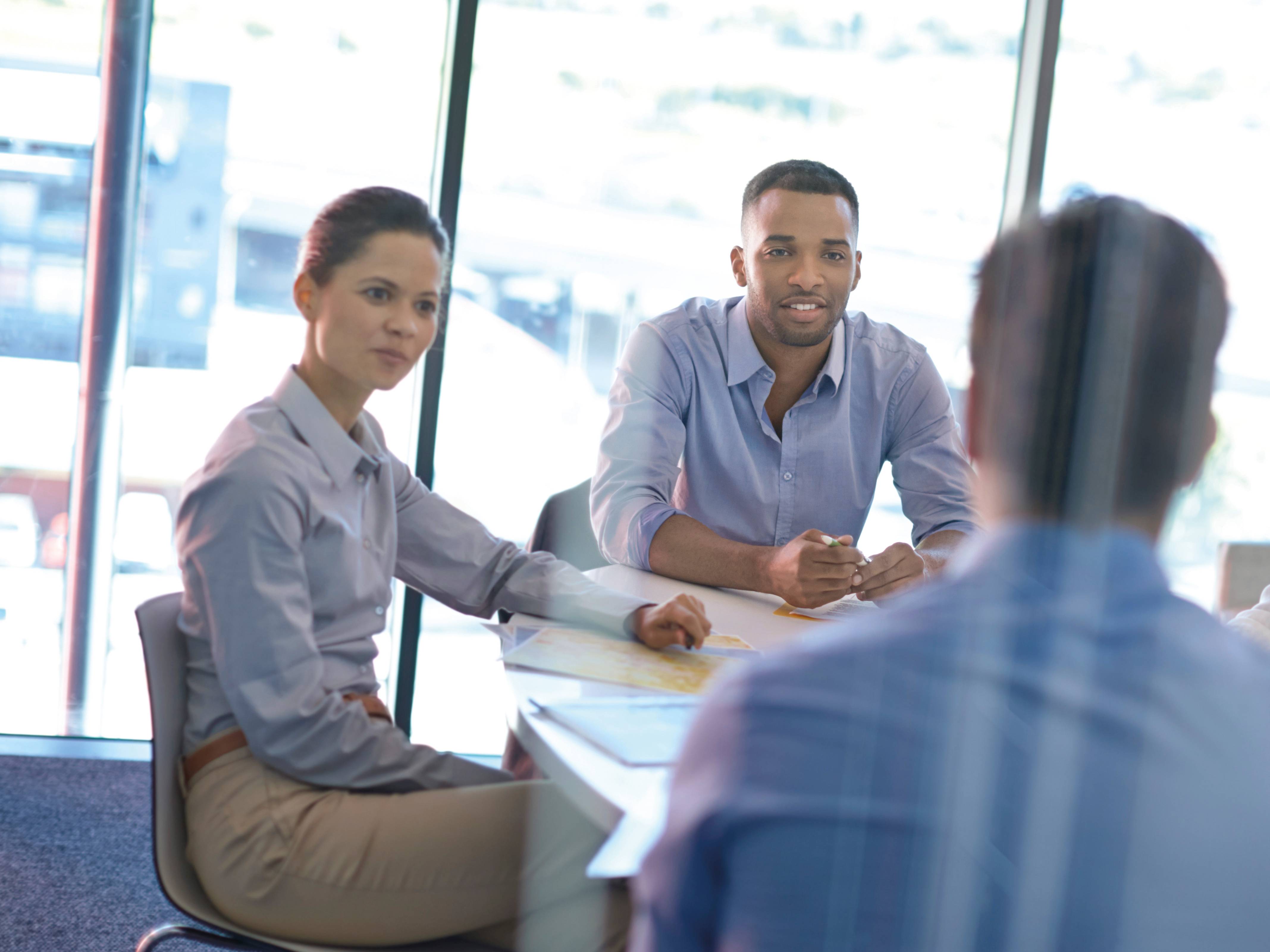 Besprechung von drei jungen Kolleginnen und Kollegen, durch eine Glaswand fotografiert.