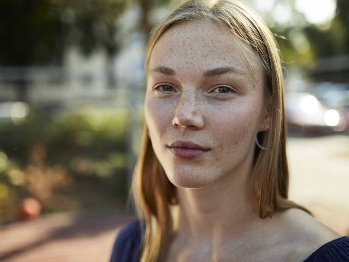 Nahaufnahme einer jungen Frau, die direkt in die Sonne schaut. Im unscharfen Hintergrund warmes Wetter.