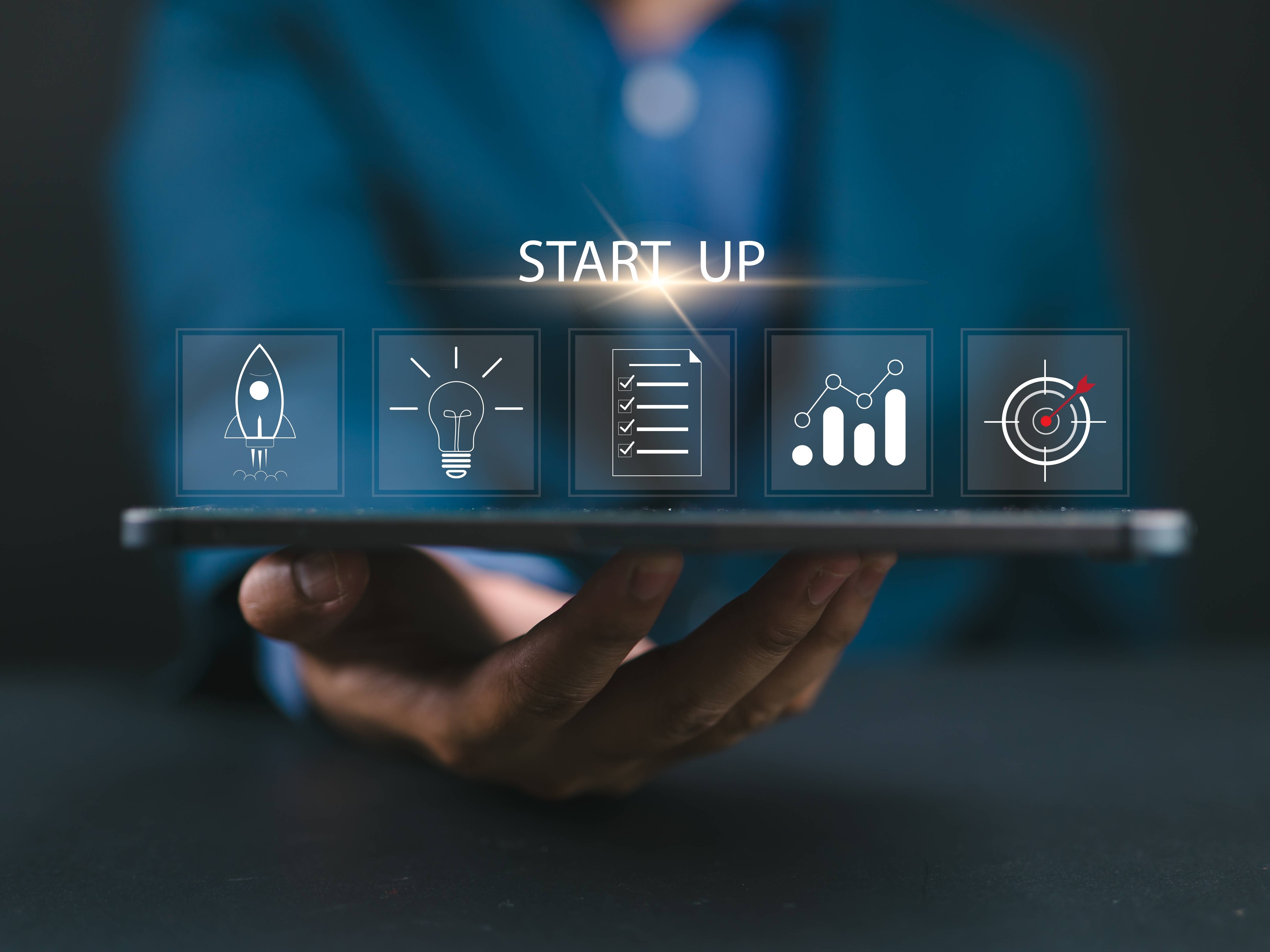 Eine HAnd hält ein Tablet. Darüber animiert Grafiken. Von links nach rechts: eine Rakete, eine Glühbirne, ein Dokument, eine Statistik, eine Zielscheibe. Darüber der Schriftzug: START UP