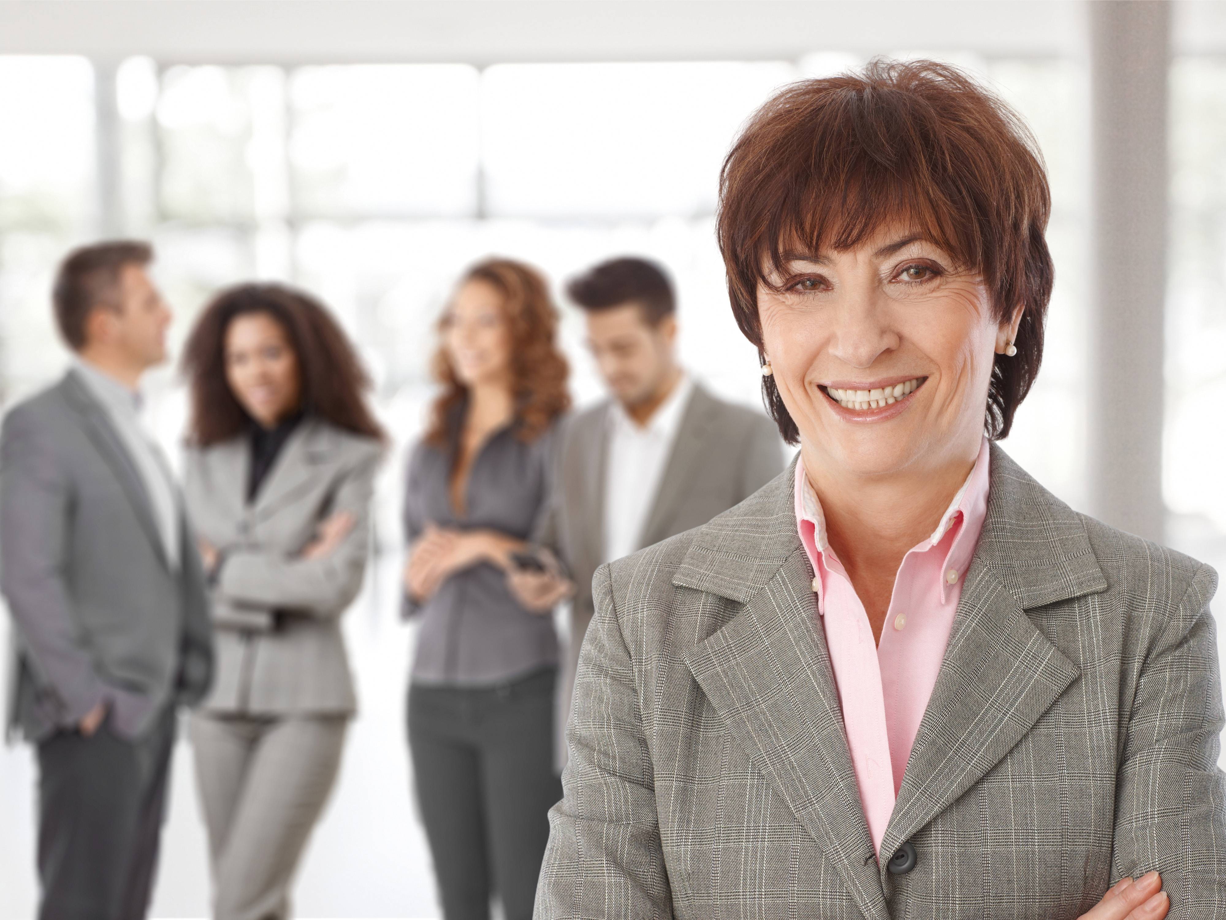 Businessfrau lächelnd im Vordergrund – dahinter ihr Team ebenfalls im Businesslook