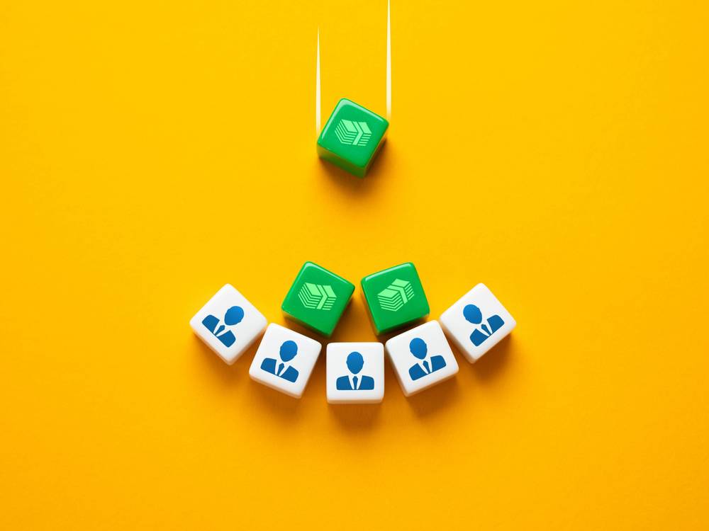 Auf gelbem Untergrund drei grüne Würfel mit Geldschein-Piktogramm und fünf weiße Würfel mit Piktogramm von Mann im Anzug. Die grünen Würfel fallen auf die weißen.