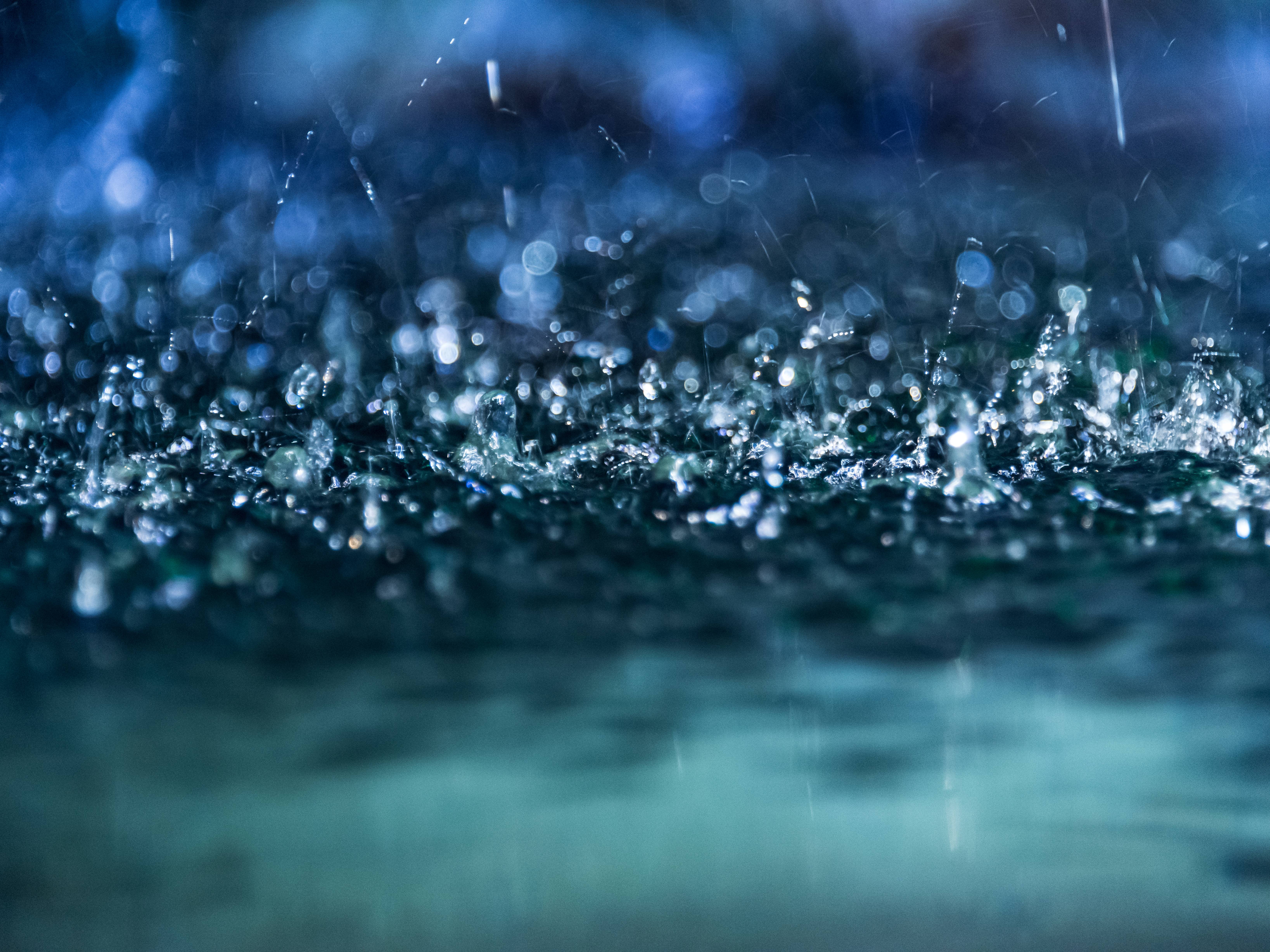 Nahaufnahme von Regentropfen, die in einer Pfütze aufkommen.