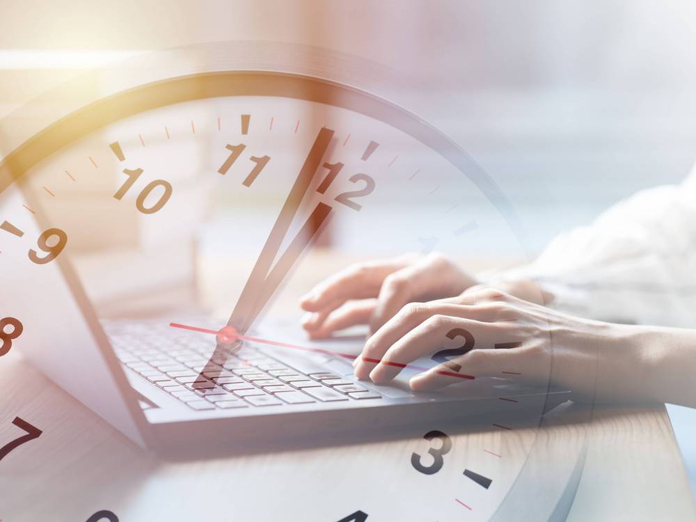 Auf der Collage zu sehen ist Uhr mit analogem Zifferblatt, die über einem Foto eines Laptops durchschimmert, auf dem getippt wird.